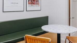A room with a green bench, a round table, and two chairs. There are two framed pictures on the wall. - Hyde Park 3BR Home with Fenced Backyard (Cincinnati)
