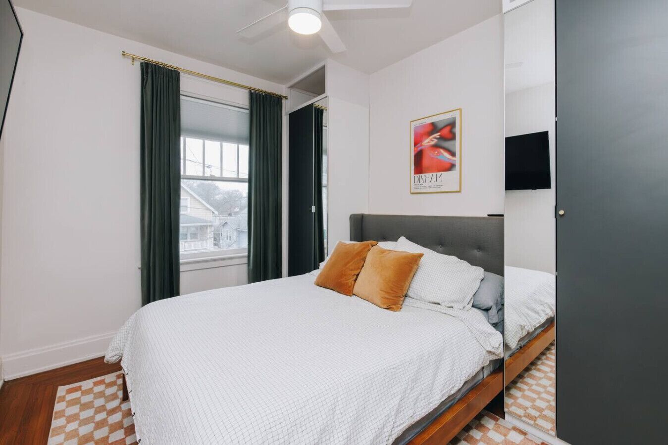 Um quarto com cama, ventilador de teto, janela com cortinas, um pôster na parede e uma porta.
