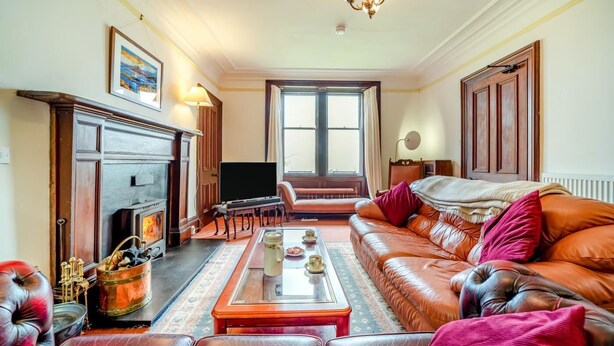 A living room with a fireplace, leather sofa, television, and a large window. - 5 Bed in Shiskine (oc-b33664) (Shiskine)