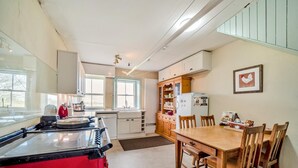 A kitchen with a red stove, a dining table with chairs, a refrigerator, and a window. - 5 Bed in Shiskine (oc-b33664) (Shiskine)