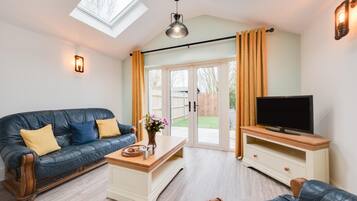 Un salon moderne avec un canapé en cuir, une table basse, un téléviseur posé sur un meuble en bois et une porte-fenêtre coulissante donnant sur un jardin.