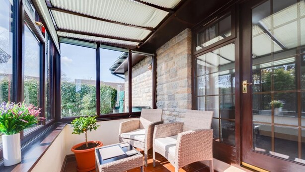En solbeskinnet balkon med fletmøbler, en potteplante og udsigt til grøn vegetation.