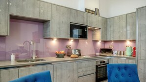 A modern kitchen with grey cabinetry, a built-in microwave, a toaster, and a kettle. There are two blue upholstered chairs and a wooden table. - 2 Bed in Whitby (oc-c33513) (Whitby)