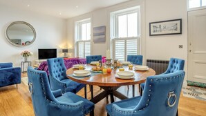 A dining area with a round table, blue upholstered chairs, and breakfast items. - 2 Bed in Whitby (oc-c33513) (Whitby)