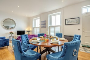 A dining area with a round table, blue upholstered chairs, and breakfast items. - 2 Bed in Whitby (oc-c33513) (Whitby)