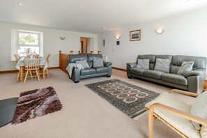 Ein Wohnzimmer mit Essbereich, zwei Sofas, einem gemusterten Teppich und einem flauschigen Teppich.