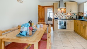 Een kleine keuken met houten kastjes, een betegelde spatwand en een eethoek met een tafel voor twee personen.