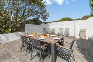 Un espace de restauration en plein air avec une table en bois, des chaises noires et un présentoir pour les fruits et les condiments.