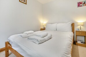 Un llit ben fet amb llençols i tovalloles blanques, un capçal de fusta, dues taules de nit amb làmpades i un quadre al mur.