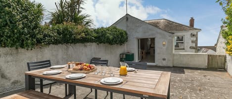 A wooden table set for breakfast with plates, cutlery, and a fruit platter, outdoors with a building in the background.
