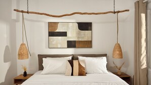 Ein Schlafzimmer mit einem Bett, zwei Nachttischen, einer Pendelleuchte und einem an der Wand hängenden, abstrakten Gemälde.