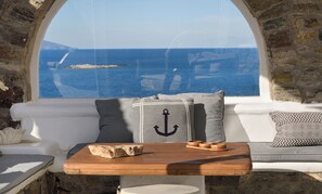 Ein gemütlicher Sitzbereich mit Blick aufs Meer, ein Holztisch mit einer Schale und eine Steinsäule.