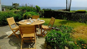 A round wooden table with four chairs, set on a patio with a view of the sea. - 3 Bed in Perranuthnoe (oc-4withe) (Perranuthnoe)