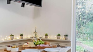 A kitchen counter with a TV, potted plants, a bottle of sparkling wine, cheese, grapes, and plates. - 1 Bed in Littlebeck (oc-m33953) (Littlebeck)