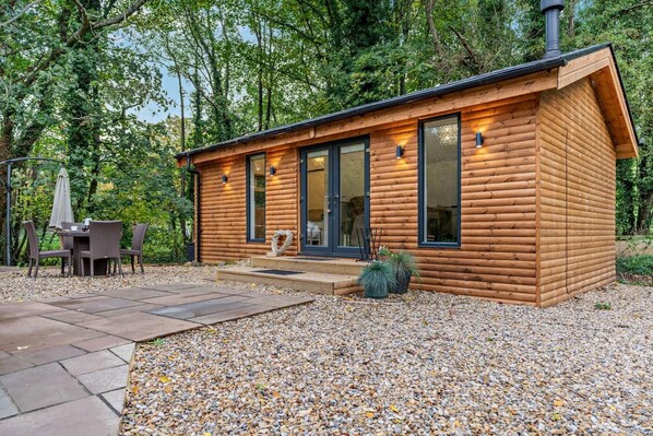 A wooden cabin with a patio, a dining set, and a chimney.