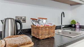 A kitchen with a stainless steel kettle, a wicker basket with food items, a loaf of bread, a sink, and a potted plant. - 1 Bed in Littlebeck (oc-m33953) (Littlebeck)