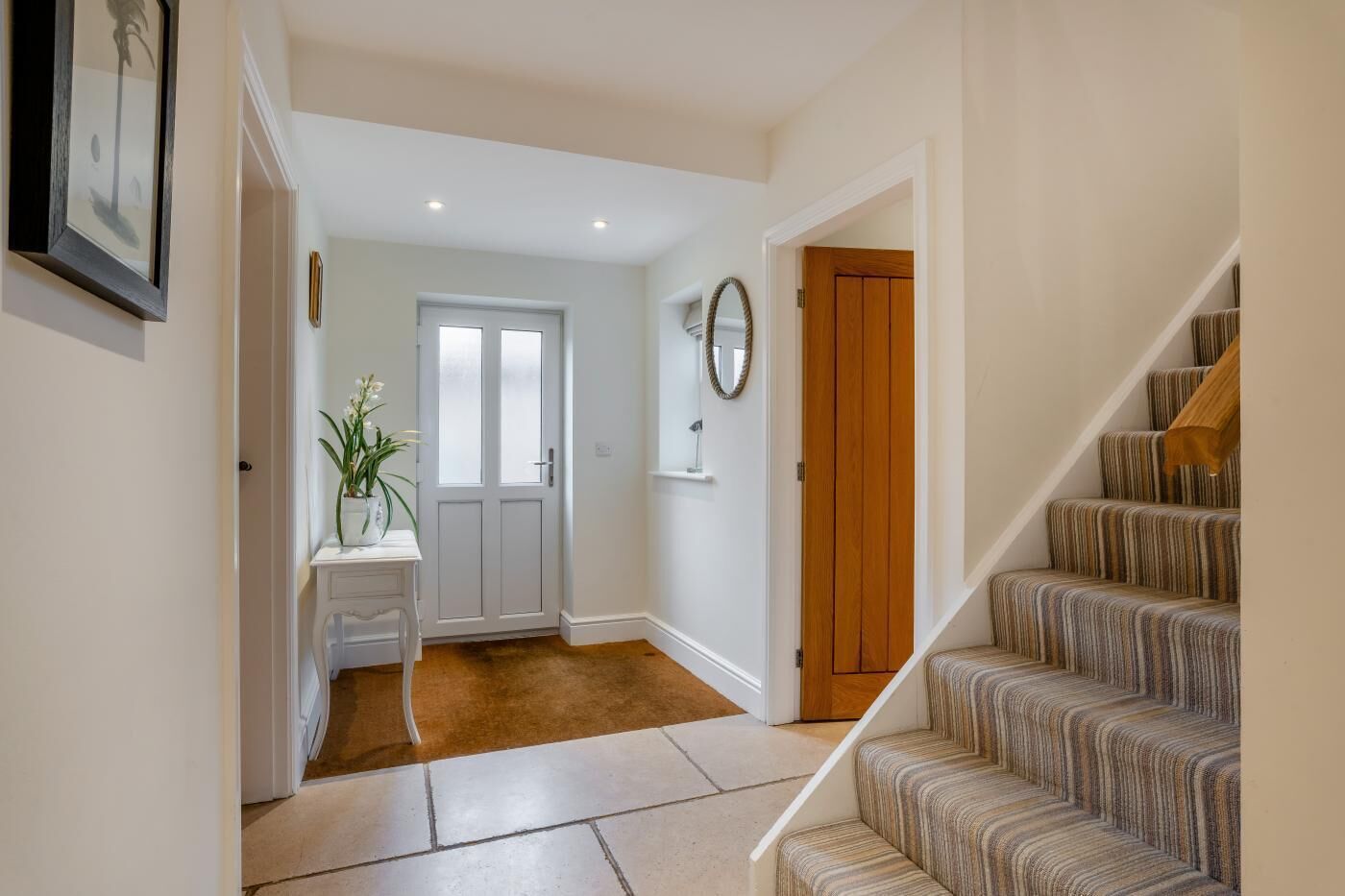 A hallway with a white door, a small table with a plant, and a staircase with striped carpet.