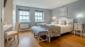 Ein Schlafzimmer mit Bett, Nachttischen, einem Sessel und Fenstern.