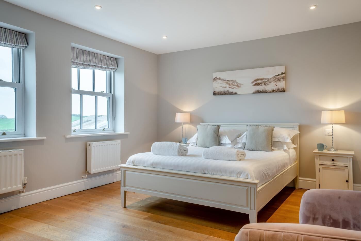 A bedroom with a large bed, two bedside tables with lamps, a window with a view, and a painting on the wall.