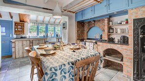 A kitchen with a brick oven, blue cabinets, and a dining area with a patterned tablecloth. - 2 Bed in Mousehole (oc-threeb) (Mousehole)