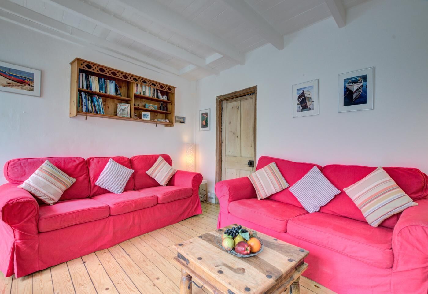 Um quarto com dois sofás vermelhos, uma mesa de centro de madeira com frutas, uma estante de madeira e quadros nas paredes.