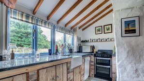 A kitchen with a large island, wooden cabinets, a built-in oven, and a view of greenery outside. - 2 Bed in Mousehole (oc-threeb) (Mousehole)