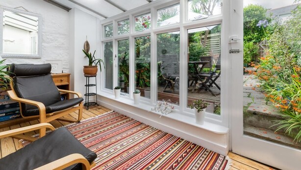 A sunroom with a large window, a wooden floor, and a black chair. - 2 Bed in Mousehole (oc-threeb) (Mousehole)