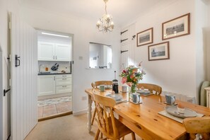 A dining area with a wooden table set for four, a chandelier, and framed pictures on the wall. - 2 Bed in Aldborough (oc-2257) (Aldborough)