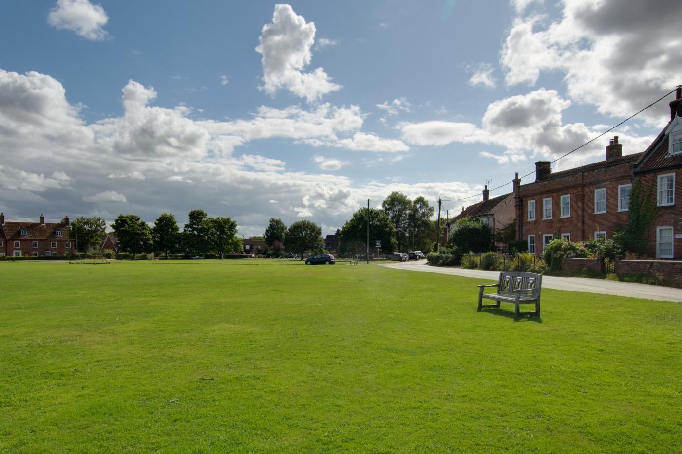A grassy field with a bench, a road, and buildings in the background.