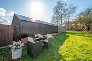 A patio with a table and chairs, a metal bucket with flowers, and a wooden fence. - 2 Bed in Aldborough (oc-2257) (Aldborough)
