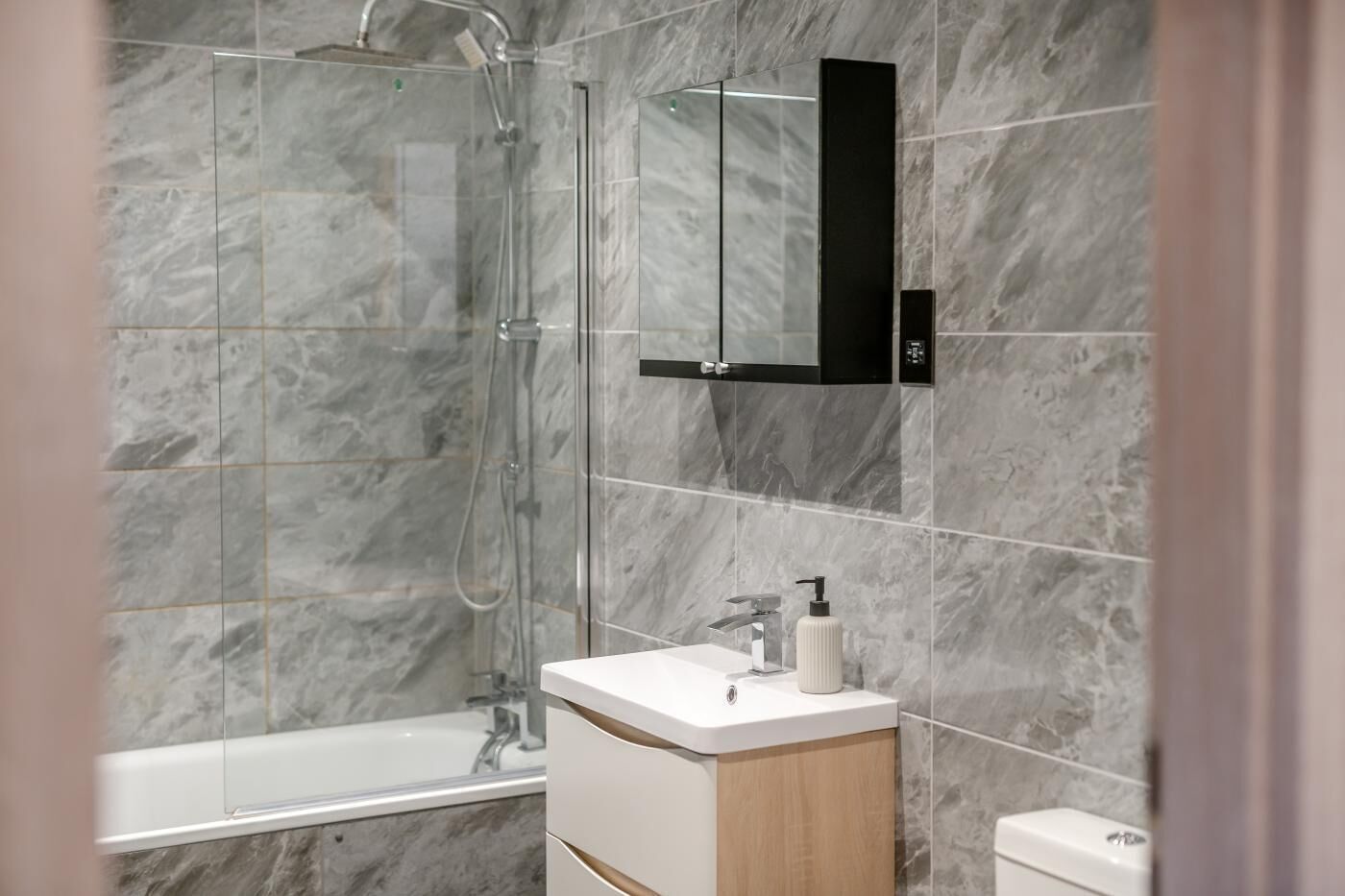A modern bathroom with a glass-enclosed shower, a white sink, and a black medicine cabinet.