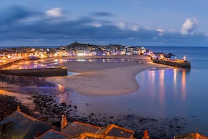 A coastal town at dusk with a beach, promenade, and buildings along the waterfront. - 3 Bed in St. Ives (oc-marhou) (St Ives)
