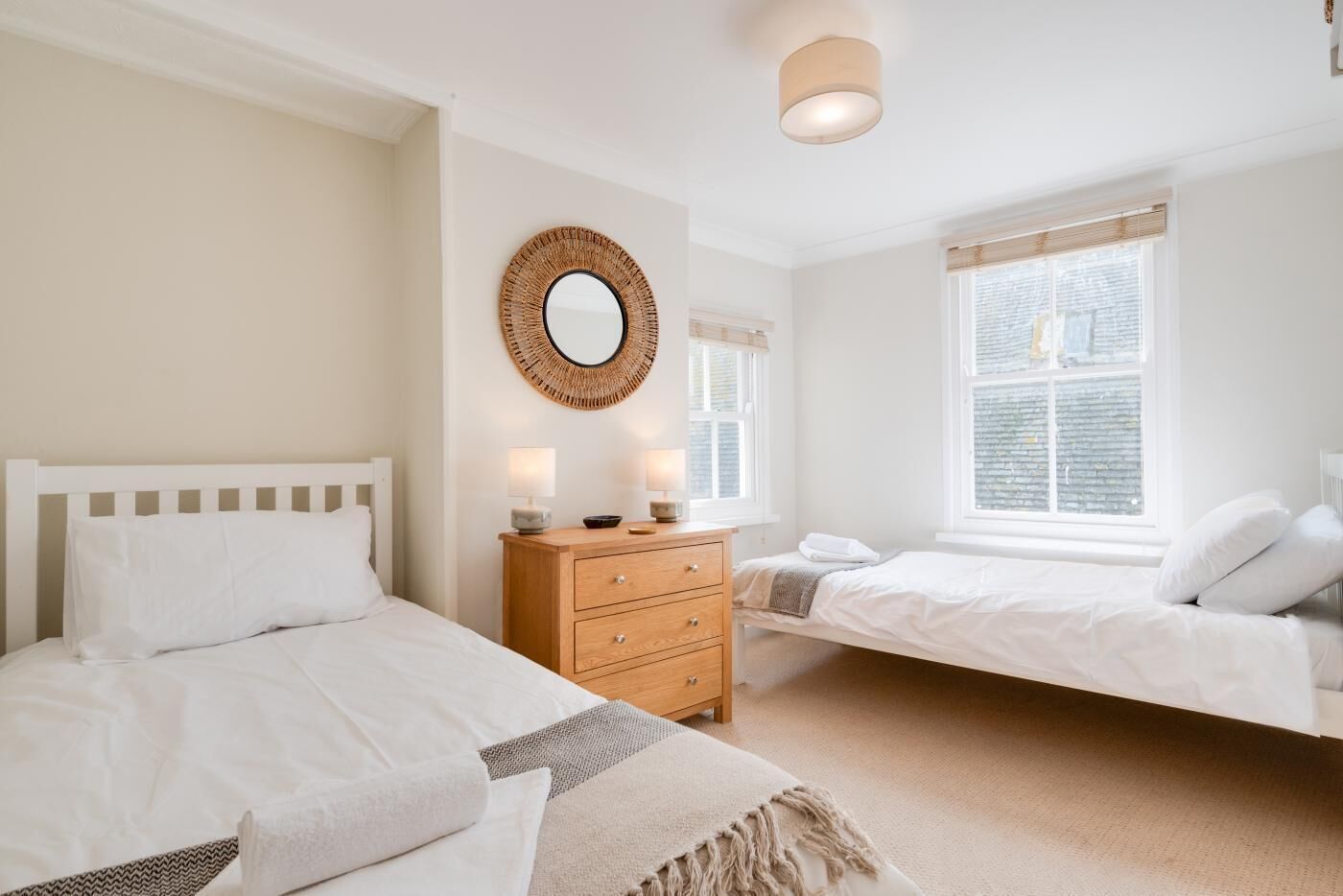 A bedroom with two beds, a wooden dresser, a mirror, and a window with blinds.