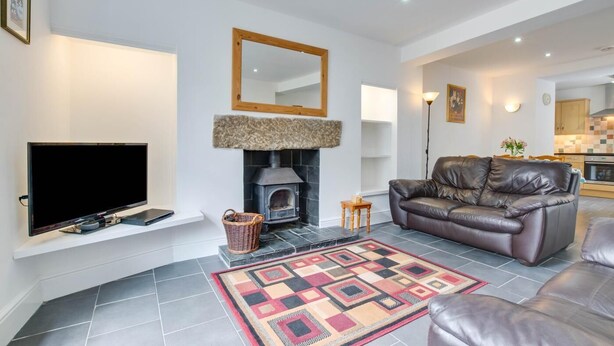 A modern living room with a fireplace, leather sofa, flat-screen TV, and a patterned rug. - 2 Bed in Mousehole (oc-carvos) (Mousehole)