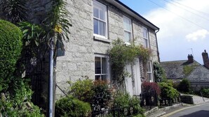 A stone building with a traditional design, featuring multiple windows and a small garden area with various plants. - 2 Bed in Mousehole (oc-carvos) (Mousehole)