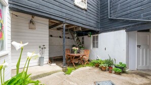 A covered patio with a table and chairs, surrounded by potted plants and a small garden area. - 2 Bed in Mousehole (oc-carvos) (Mousehole)