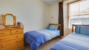 A bedroom with two single beds, a wooden dresser, a mirror, and a window with blinds. - 2 Bed in Mousehole (oc-carvos) (Mousehole)