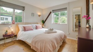 Une chambre avec un grand lit, des tables de chevet, une commode et deux fenêtres.