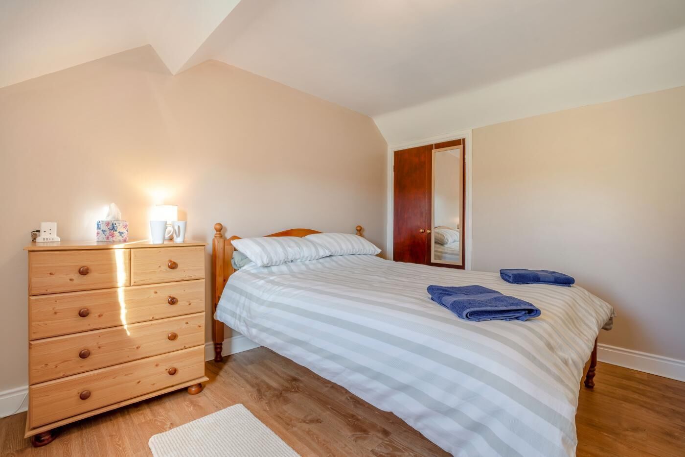 A bedroom with a bed, wooden dresser, and a mirror on the wall.