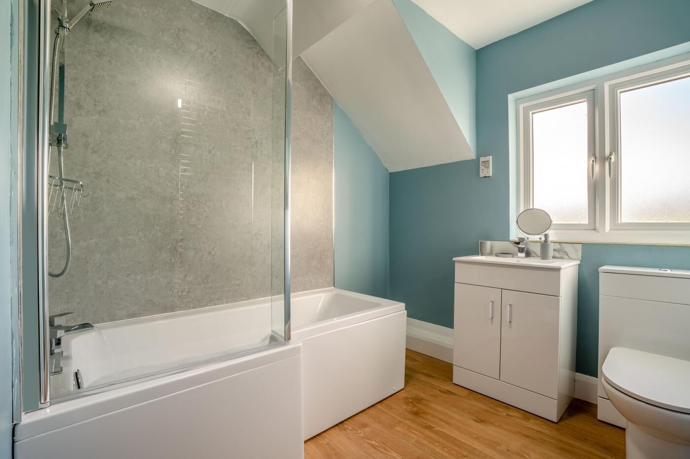 Un baño moderno con ducha de vidrio, una bañera blanca, un inodoro blanco y un tocador con espejo.