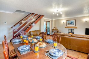 A dining area with a wooden table set for breakfast, a staircase, a leather sofa, and a fireplace. - 3 Bed in Marske (oc-o33522) (Marske)