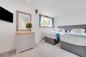 A bedroom with two beds, a dresser, a mirror, a TV, and a window with curtains. - 4 Bed in Saundersfoot (oc-pw9262) (Saundersfoot)