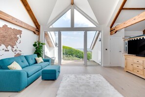 A modern living room with a large window, a blue sofa, a white rug, and a wooden cabinet. - 4 Bed in Saundersfoot (oc-pw9262) (Saundersfoot)