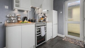 Una cuina compacta amb armaris blancs, forn de pared i nevera.