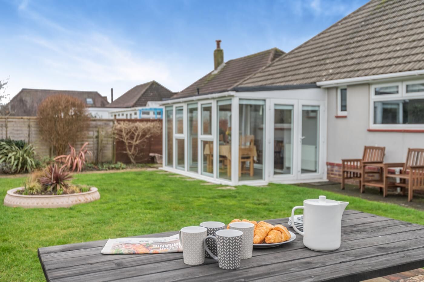 A patio with a table set for breakfast, including croissants and a newspaper.
