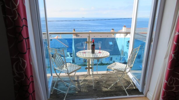 En balkon med et bord og to stole, udsigt over vand og bygninger.