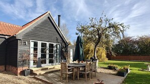Une terrasse en bois avec une table et des chaises, un pot de fleurs et un arbre dans un jardin.
