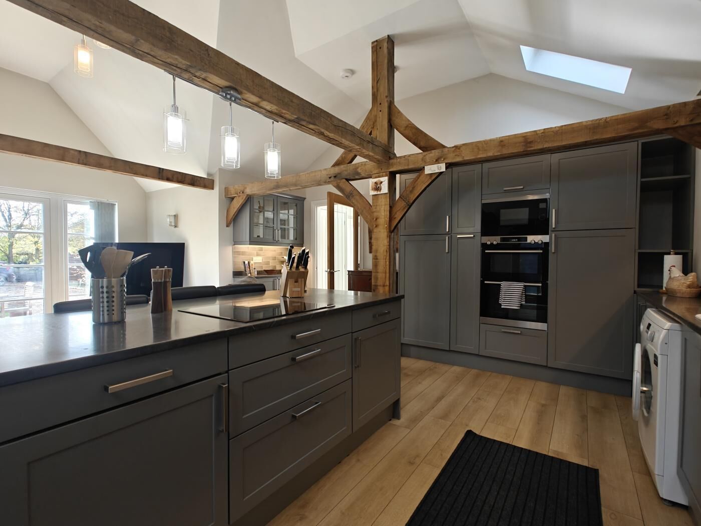 A modern kitchen with dark cabinetry, wooden beams, and a skylight.