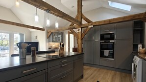 Une cuisine moderne avec des meubles de couleur sombre, des poutres en bois et une lucarne.
