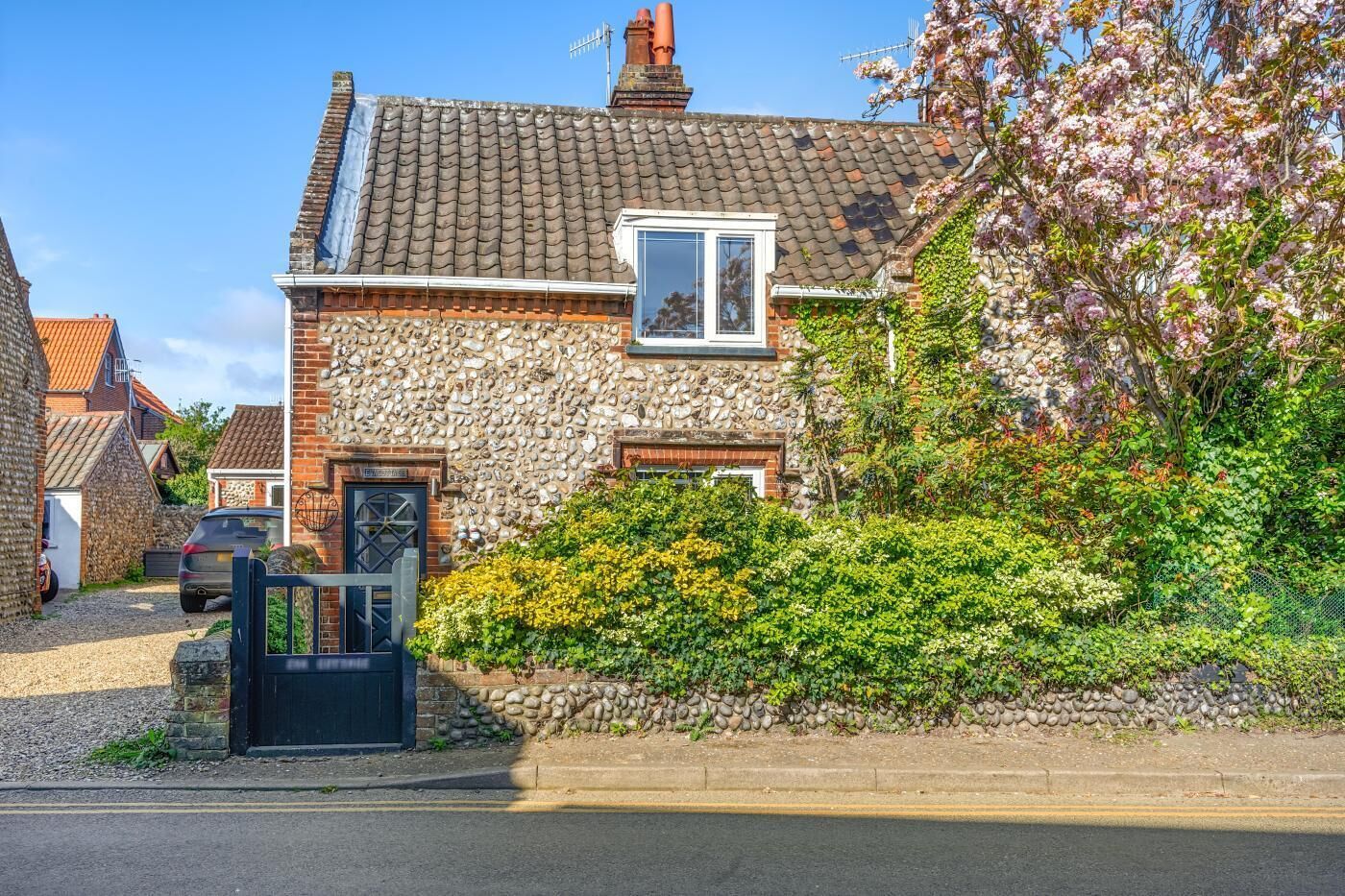 A stone house with a tiled roof, a small window, and a garden with flowering plants.